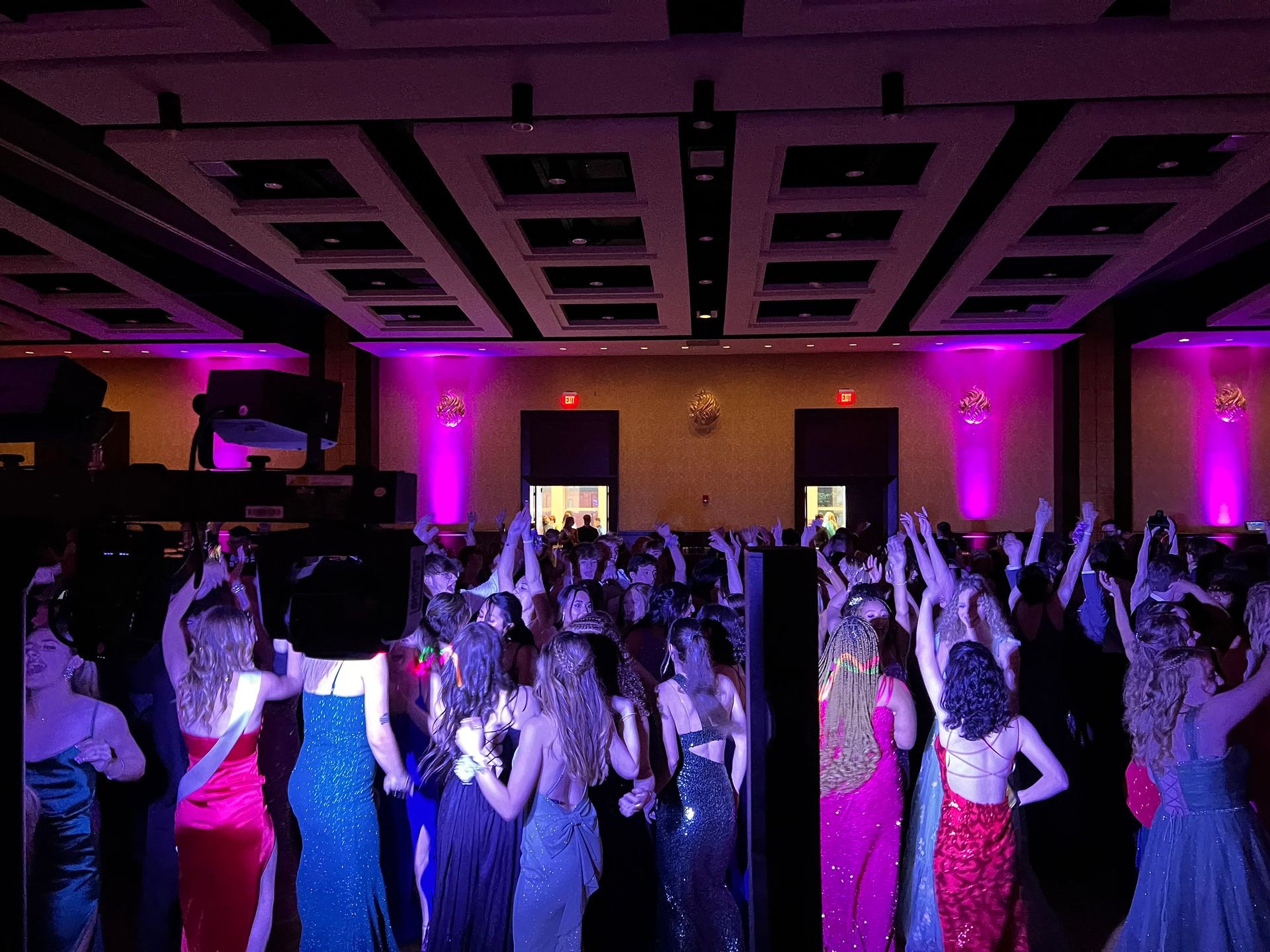 Crowd of people in formal attire dancing and celebrating under purple lighting at an indoor event.